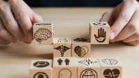 Hands arranging wooden blocks with healthcare and medical symbols including brain, heart, caduceus on desk for wellness concept design.