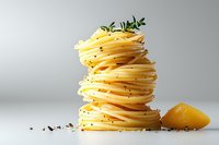 Cooked spaghetti pasta neatly stacked in twisted tower formation with fresh herbs, black pepper and lemon on light background, minimalist food composition.