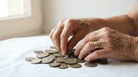 Senior man with wrinkled hands counting coins on white surface, representing financial planning, savings, retirement budgeting, and money management for older adults.