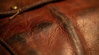 Brown leather texture with natural grain and stitching details. Vintage craftsmanship showing worn surface patterns and aged material for luxury goods design.