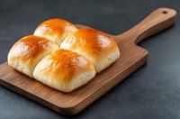 Fresh homemade dinner rolls with golden brown crust served on wooden cutting board against dark background, soft and fluffy bread buns for restaurant menu.