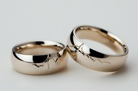 Two cracked gold wedding rings symbolizing broken marriage, divorce concept, relationship problems, separation and marital issues on white background.
