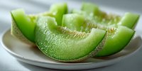Fresh slices of green honeydew melon arranged on white plate, showcasing juicy flesh and textured rind for healthy summer refreshment.