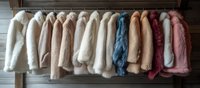 Collection of trendy faux fur coats in pastel and neutral colors hanging on wooden rack against rustic wall background, fashion retail display arrangement.