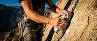 Rock climber gripping granite cliff face with muscular hands and climbing gear against mountain landscape background for outdoor adventure sports.