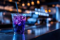 Purple cocktail with ice and straw on bar counter at night, blurred city lights in background. Suitable for beverage, nightlife, and hospitality design projects.