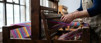 Skilled artisan weaving colorful textile on a traditional wooden loom in a rustic workshop, showcasing handcraft and heritage fabric art.