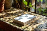 Book lying on floral patterned tablecloth near window with natural sunlight casting shadows, creating cozy reading atmosphere in home interior setting.