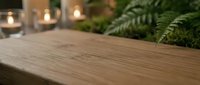 Wooden table surface with blurred green ferns and candles in soft background, suitable for home decor and lifestyle content.