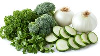Fresh green vegetables and herbs on white background including broccoli florets, sliced cucumber, white onions and curly parsley arranged in composition.
