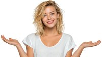 Young blonde Caucasian woman with wavy hair smiling and gesturing with open palms in welcoming pose, wearing casual white v-neck t-shirt on white background.