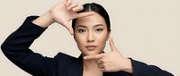 Young Asian businesswoman making frame gesture with hands against beige background for creative composition and visual storytelling concepts.