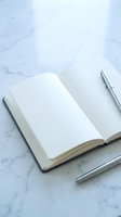 Open blank notebook with silver pen on white marble surface for writing, journaling, planning and creative work projects.