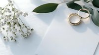 Gold wedding rings with baby's breath flowers and eucalyptus leaves on white invitation card. Elegant wedding stationery setup for marriage ceremony.