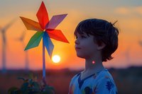 Young boy looking at colorful pinwheel windmill against beautiful orange sunset sky, capturing childhood wonder and dreams in magical evening light.