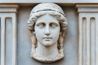 Ancient Roman marble sculpture head of young woman with braided hair and diadem mounted on classical architectural wall relief for historical education.