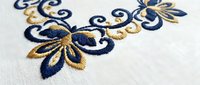Elegant blue and gold floral embroidery on white fabric with decorative swirls and leaves pattern for luxury textile design and crafting projects.