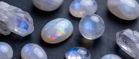 Collection of natural moonstone and crystal gemstones with iridescent blue flash adularescence effect on dark surface for jewelry making and healing.