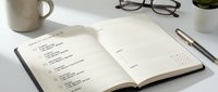 Open planner notebook with handwritten to-do list on white desk with coffee mug, glasses and pen for productivity and organization planning.