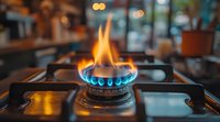 Blue and orange flames burning on gas stove burner in kitchen, close up view with blurred background showing warm ambient lighting and cozy home atmosphere.