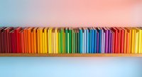 Colorful books arranged in rainbow spectrum on wooden shelf against gradient background for education and learning concepts.