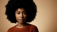 Young African American woman with natural afro hairstyle wearing rust colored sweater against warm beige background for lifestyle and beauty content.