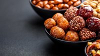 Assorted energy balls with nuts, dates, and sesame seeds served in black ceramic bowls on dark background. Healthy vegan protein snacks for fitness nutrition.