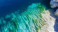 Aerial view of crystal clear turquoise water meeting white limestone shore with natural wave patterns and ripples creating abstract texture in tropical coastline.