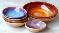 Handcrafted ceramic bowls in earthy terracotta and cosmic galaxy glazes arranged on light surface, showcasing artisanal pottery collection for dining and home decor.
