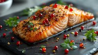 Grilled salmon fillet with herbs, spices and pomegranate seeds on dark slate board, macro food photography with selective focus and garnish.