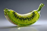 Creative glass art banana-shaped kiwi fruit hybrid sculpture with vibrant green color and black seeds against gray background, showcasing unique food-inspired design.