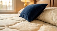 Luxurious bedroom setting with navy blue velvet pillow on cream quilted bedding, warm golden lighting, and elegant interior design for home decor projects.