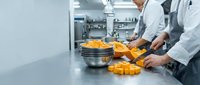 Professional chefs preparing fresh pasta in modern commercial kitchen with stainless steel equipment and organized workspace for culinary food preparation.