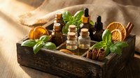 Natural essential oils collection in wooden box with fresh herbs, dried orange slices and cinnamon sticks for aromatherapy and wellness treatments.