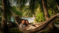 Happy couple relaxing together in hammock between palm trees on tropical beach paradise vacation getaway for romantic honeymoon retreat.