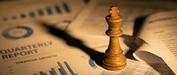 Wooden chess king piece positioned on quarterly business report with financial charts and graphs representing strategic planning and corporate leadership success.