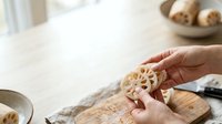 Hands holding sliced lotus root on wooden cutting board in bright kitchen. Food preparation and cooking concept for culinary, recipe, and ingredient content.