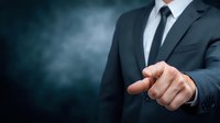 Businessman in dark suit pointing finger against smoky blue background, conveying leadership and decision-making in corporate environment.