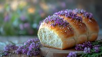 Fresh baked brioche bread loaf decorated with purple lilac flowers on rustic wooden surface against blurred garden background, soft natural lighting.