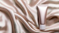 Luxurious cream tube on elegant draped silk fabric in soft beige and rose gold tones. Cosmetic product mockup against flowing satin background for beauty branding.