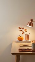 Cozy autumn workspace with copper desk lamp illuminating orange pumpkin and fall leaves in vase on wooden desk with books and warm lighting for seasonal decor.