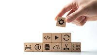 Hand placing wooden cube with gear icon completing technology stack on white background for business automation and software development concepts.