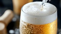 Fresh cold beer being poured into glass with frothy white foam head and rising bubbles, golden liquid catching light against dark background. Refreshing drink macro.