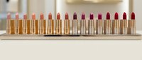 Row of luxury lipsticks in golden tubes displaying gradient color palette from nude to deep red shades on marble surface for cosmetic branding.