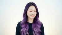Young Asian woman with long wavy purple ombre hair, eyes closed, serene expression, wearing black top on light background, hair color salon concept.