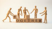Wooden mannequins holding hands and arranging letter blocks spelling together, representing teamwork, collaboration, unity and cooperation for business concepts.