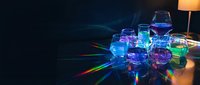 Colorful glass laboratory beakers and flasks with vibrant blue and green liquids creating rainbow light reflections on dark surface for science education.