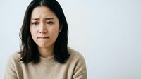 Young Southeast Asian woman with long dark hair wearing a beige sweater, displaying a sad or disappointed facial expression against a white background for emotional portraiture.