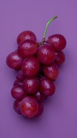 Fresh red grape cluster with water droplets on purple background, minimalist food composition highlighting natural texture and juicy appearance.