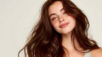 Young woman with flowing brown hair and natural makeup smiling confidently against neutral beige background, perfect for beauty and skincare advertising.